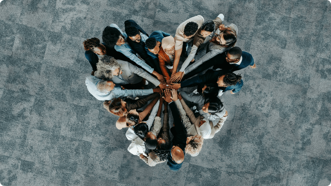 Diverse team huddling, hands stacked together in the center, viewed from above.